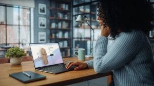 A consumer shops online from home, looking at a dress on their laptop.